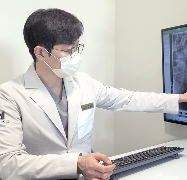 The clinician reviews a dental X-ray on the screen. Actual clinic photograph.